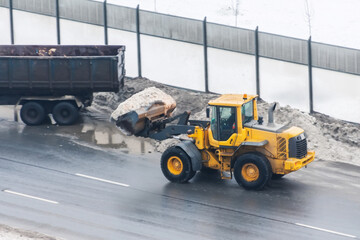 Tractor with a bucket of snow loads into the back of a truck.