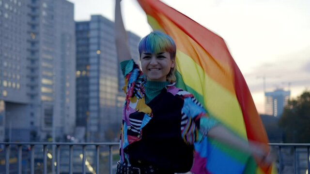 Happy non-binary person waving rainbow flag
