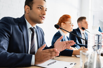 Obraz premium Indian politician gesturing, while speaking in microphone in boardroom with blurred colleagues on foreground