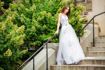 Fototapeta premium Beautiful girl wearing white wedding dress posing alone on the chapel stairs