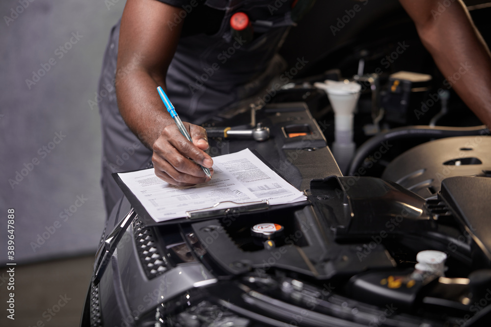 Wall mural african professional auto service technician in uniform standing near car hood repairing and using c