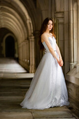 Fototapeta premium Beautiful girl wearing white wedding dress posing alone at a castle hall