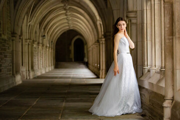 Beautiful girl wearing white wedding dress posing alone at a castle hall