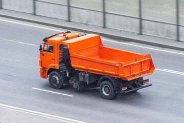 An orange dump truck with an empty body and a road cleaning brush drives on the highway.