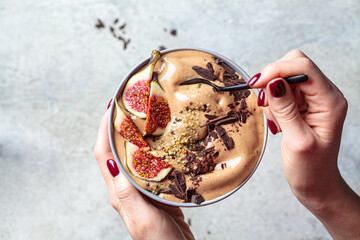 Woman holding a bowl of chocolate smoothie with figs and hemp seeds, gray background. Healthy vegan...