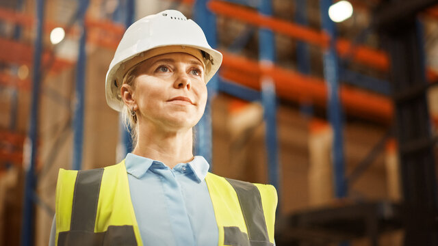 Portrait of the Beautiful Female Warehouse Inventory Manager Smiling Charmingly with Rows of Shelves Full of Merchandise, Goods and Products Packed in Cardboard Boxes Ready for Shipment. 
