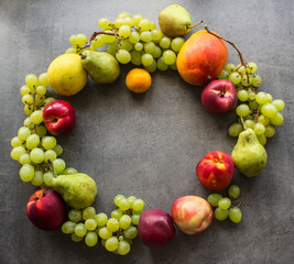 Summer fruit composition. Colorful grapes, nectarines, mango and pears wreath top view photo. Dark grey textured background with copy space. 