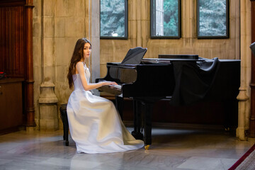 Portrait of a beautiful girl wearing white wedding dress at the piano playing