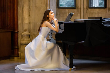Portrait of a beautiful girl wearing white wedding dress sitting at the piano and dreaming