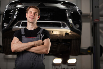 Naklejka na ściany i meble portrait of pleasant auto mechanic posing at camera, smiling. automobile in the background