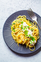 Spaghetti pasta with ricotta and fresh basil in gray plate, top view.