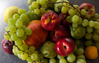 Beautiful fresh fruits on dark grey table: green grapes, nectarines, apricot. Summer fruits top view. 
