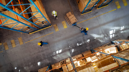 Top-Down View: In Warehouse People Working, Forklift Truck Operator Lifts Pallet with Cardboard...