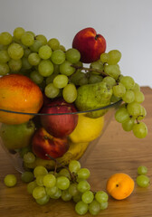 Fresh summer fruits in a glass vase. Colorful still life with grapes, mango, bananas, pears, peaches, nectarines and apricots on a table. 
