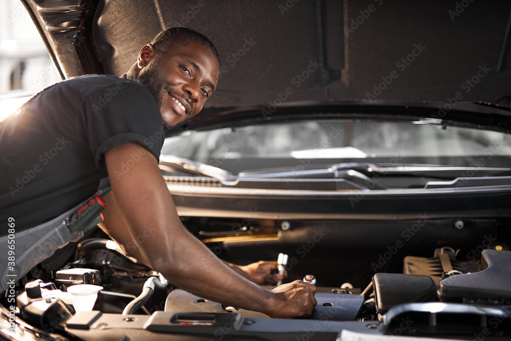 Wall mural handsome guy repairing auto's hood, using tools. wearing unifrom, concentrated on work