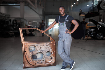 young african auto mechanic at work with separate part of the machine, posing at camera, going to repair
