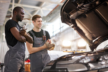 two friendly professional auto mechanic during work, they are successfully repairing car, solve...