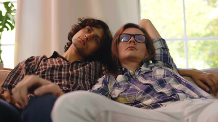 Young gay couple sitting on couch and cuddling at home