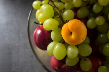 Fresh summer fruits in a glass vase. Colorful still life with grapes, mango, bananas, pears, peaches, nectarines and apricots on a table. 