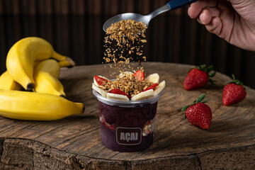 Delicious Brazilian Açaí Cream, in a plastic Cup With Strawberry, banana and granola Topping, in a rustic wooden background. Summer acai smoothie