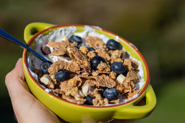 Hand of a man holding healthy breakfast with greek yogurt, muesli and blueberries in a green bowl. 