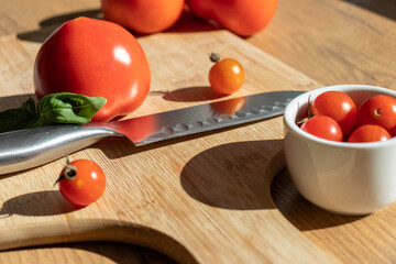 Fresh tomato on a cutting desk with knife and cherry tomatoes in a small bowl. 