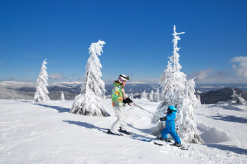 little boy and teen girl skiing in snowy mountains with helmet, goggles. Ski lessons from an older sister to brother