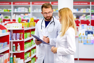 confident male and female druggists talk in pharmacy, professional pharmacists talk about the attributes and side effects of a medicine or pharmaceutical product for sale