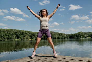 Athletic woman doing sports outside on a hot summer day. Healthy lifestyle. On the background of a large lake.