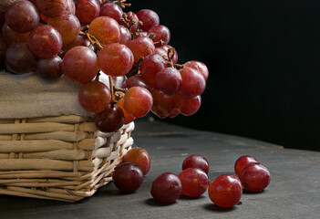Red grapes in a basket with a black background on a dark wooden table, still life, baroque renaissance or dark food photography style, with a  moody light