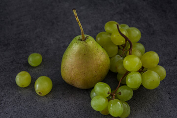 Still life with green pears and grapes on dark grey textured background. Summer fruits close up photo. 