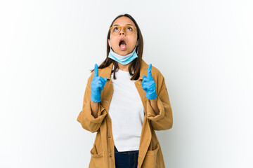 Young latin woman wearing a mask to protect from covid isolated on white background pointing upside with opened mouth.