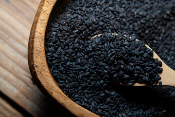 Heap of black Sesame close-up shot on a wooden spoon and in wooden bowl, wooden background