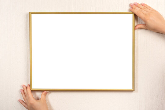 Golden blank picture frame hanging on a beige wall. Hands hanging photo frame mockup on wall