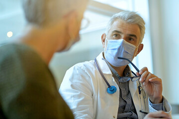Fototapeta na wymiar Doctor with face mask listening to patient in office, 19-ncov pandemic
