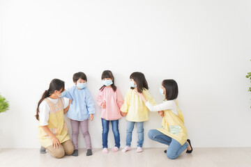 マスクを付けて幼稚園で遊ぶ子どもたちの先生
