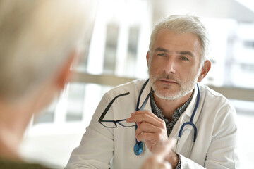 Mature practitioner in office listening to patient