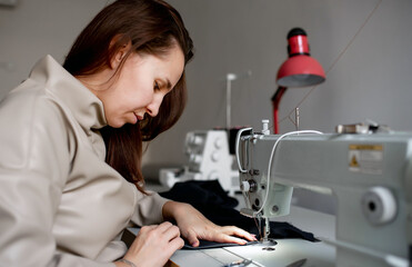 A woman sews a dark fabric on a sewing machine. Design studio, tailoring process concept.