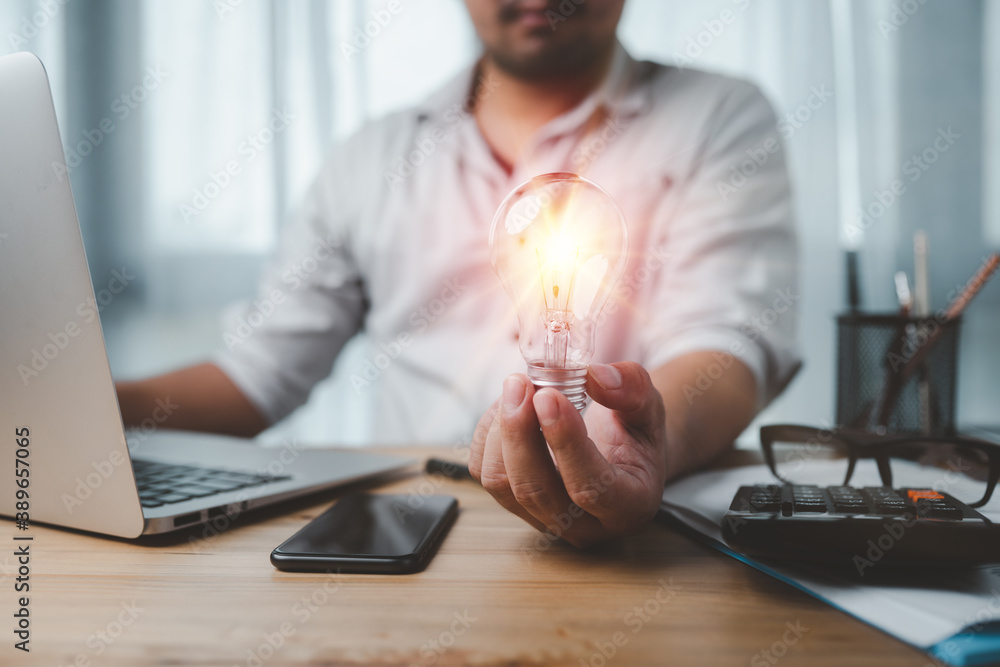 Leinwandbilder male hand holding a light bulb and he is using a notebook computer. the idea of ​​inspiration from o