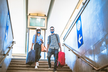 Multiracial young friends with face mask walking down a stair in train station, in the coronavirus...