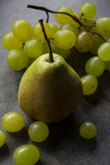 Still life with green pears and grapes on dark grey textured background. Summer fruits close up photo. 
