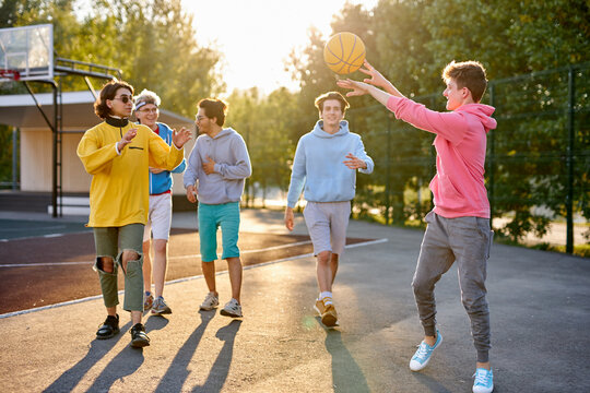 energetic, healthy teens have fun, talk before playing basketball, group of happy teenage boys in colourful casual wear, playing basketball outdoors in the city, go at playground