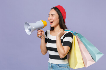 Funny young asian woman 20s in striped t-shirt red beret standing hold package bags with purchases...