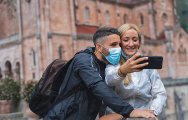 A young couple take a selfie with a mask against the COVID 19 in front of a monument in Spain.