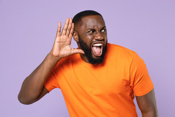 Shocked curious young african american man 20s wearing basic casual orange blank empty t-shirt try...