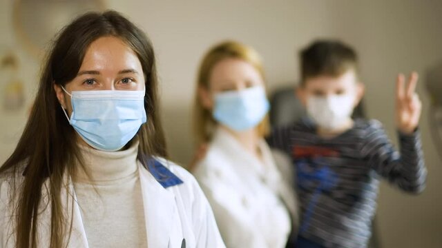 Happy mother stands behind eye doctor in face mask holding son
