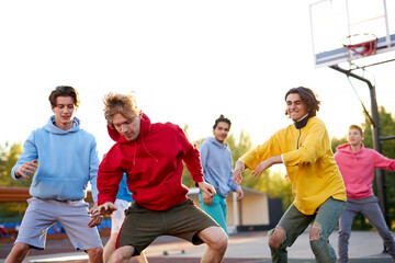 group of young male teenagers in colourful hoodies playing basketball outdoors in the street