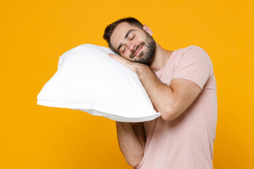 Smiling sleeping young bearded man 20s in pajamas home wear hold in hands pillow while resting at...