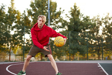 young caucasian teen boy playing basketball, handsome guy in casual sportswear alone at basketball playground, practice