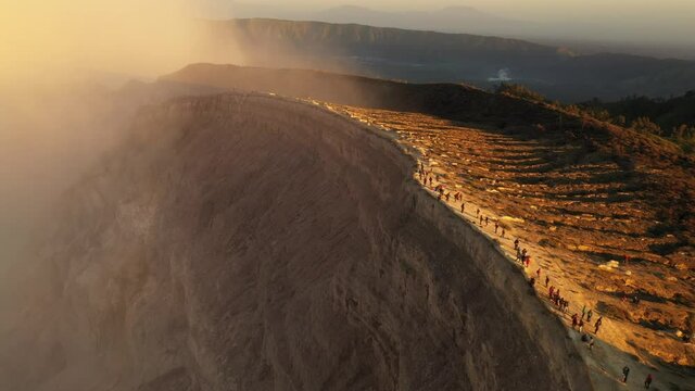 Aerial flyby along the ridge of Ijen volcanic crater. hikers walking along the edge of Ijen crater, then overlooking the cliff edge onto the mysterious depths below. Java Island, Indonesia.